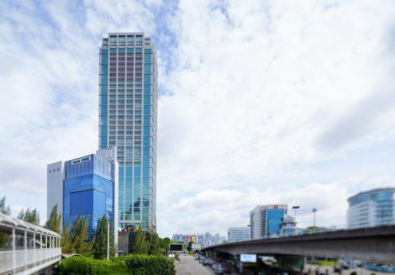 Exterior view of the glass-facade Grand Slipi Tower under a bright cloudy sky.