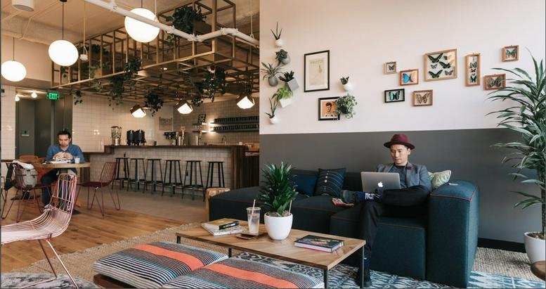 Spacious communal lounge at 22 Cross Street, Singapore featuring a cafe bar, hanging plants, and cozy seating.