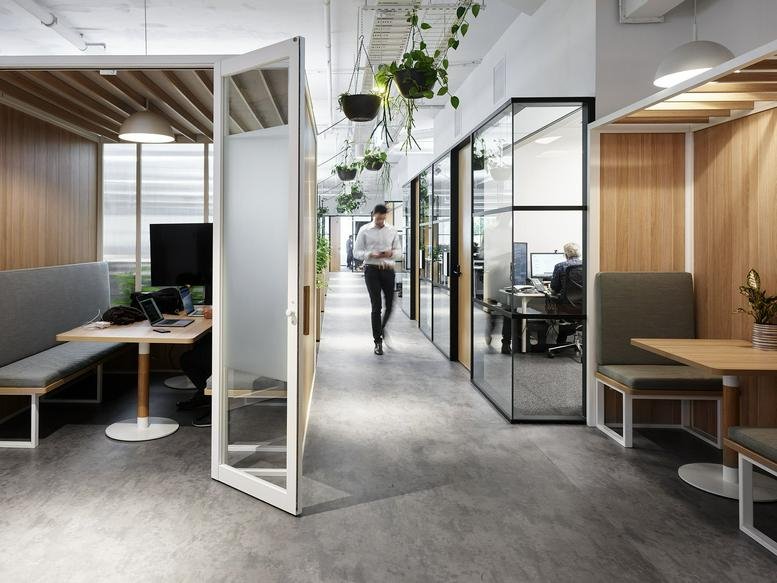 Modern office hallway featuring private phone booths and glass-walled meeting rooms.
