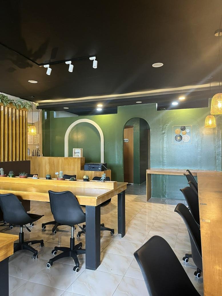 Modern coworking space with wood-top communal desks, black rolling chairs, and a green feature wall.