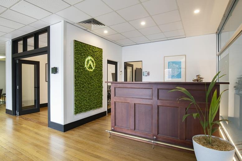 Wooden reception desk featuring a green moss wall and framed art.