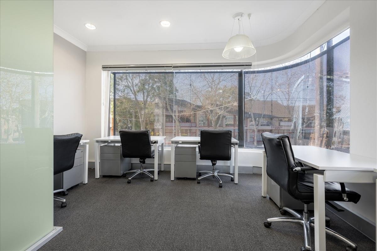 Bright workspace at 246 Pacific Highway, Crows Nest featuring desks by large windows with leafy views.