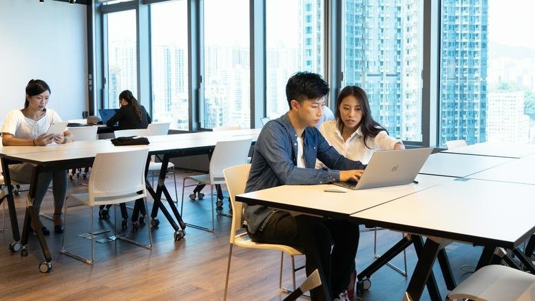 People working in a bright communal workspace with city views at Dah Sing Financial Centre.