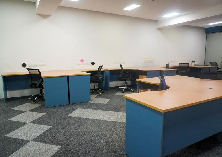 Co-working area at Co Base Workspace, 25 Jalan Pandak Mayah 5 featuring desks with blue bases and black chairs.