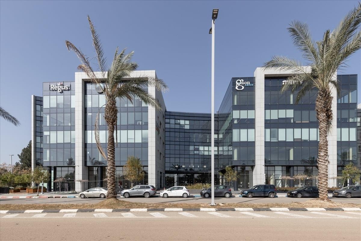Exterior view of the glass-facade 3 Ariel Sharon Street building with palm trees and a blue sky.