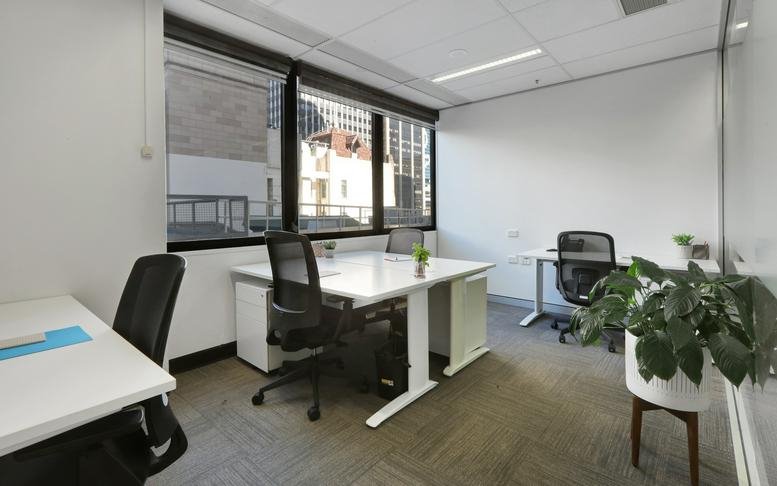 Large open workspace featuring rows of white desks and ergonomic black chairs.