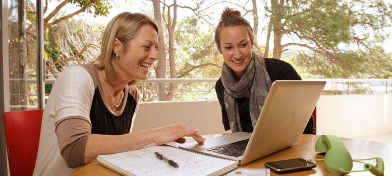 Two women smiling while working on a laptop at 339/341 Barrenjoey Road, Sydney.