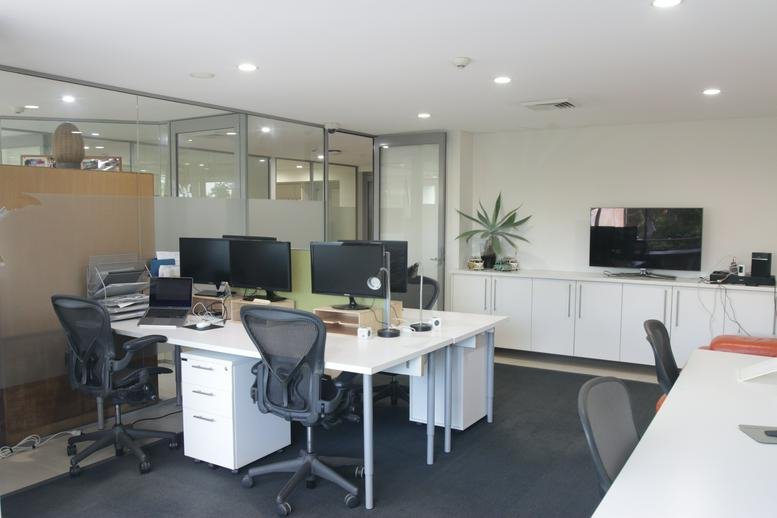 Spacious open-plan office featuring multiple workstations, white desks, and large flat-screen monitors.