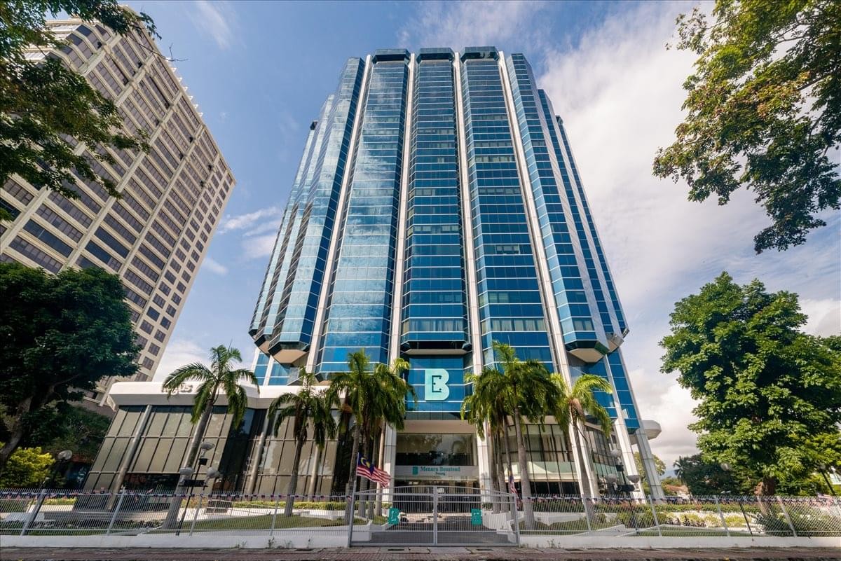 Exterior view of the glass-facade Menara Boustead with palm trees in the foreground.