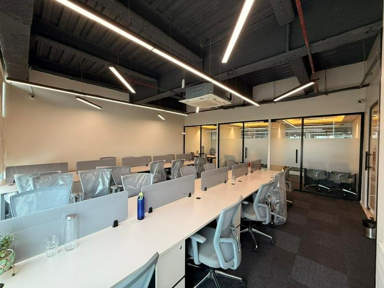 Spacious workstation area with long white desks, ergonomic grey chairs, and bright linear lighting.