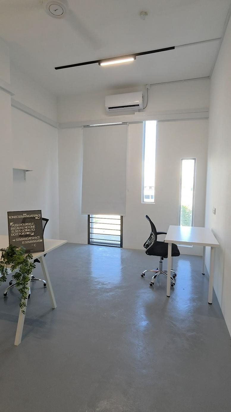 Modern interior office at Semangat Space, Suite 43-02, featuring clean white desks and grey flooring.