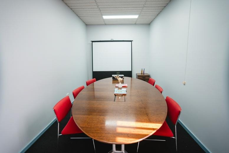 Spacious boardroom at Westend Business Hub featuring a long oval wood table and red chairs.