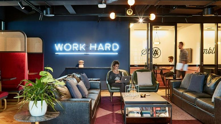 Lounge area with blue neon Work Hard sign, leather sofas, and indoor plants at 5 Martin Place, Sydney NSW 2000.