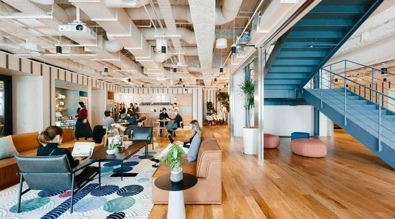 Spacious open-plan workspace featuring industrial ceilings, wooden floors, and a large blue feature staircase.