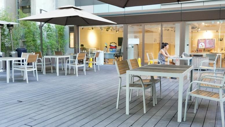 Spacious outdoor terrace at Base Strand 50 with grey decking, white tables, and large umbrellas.