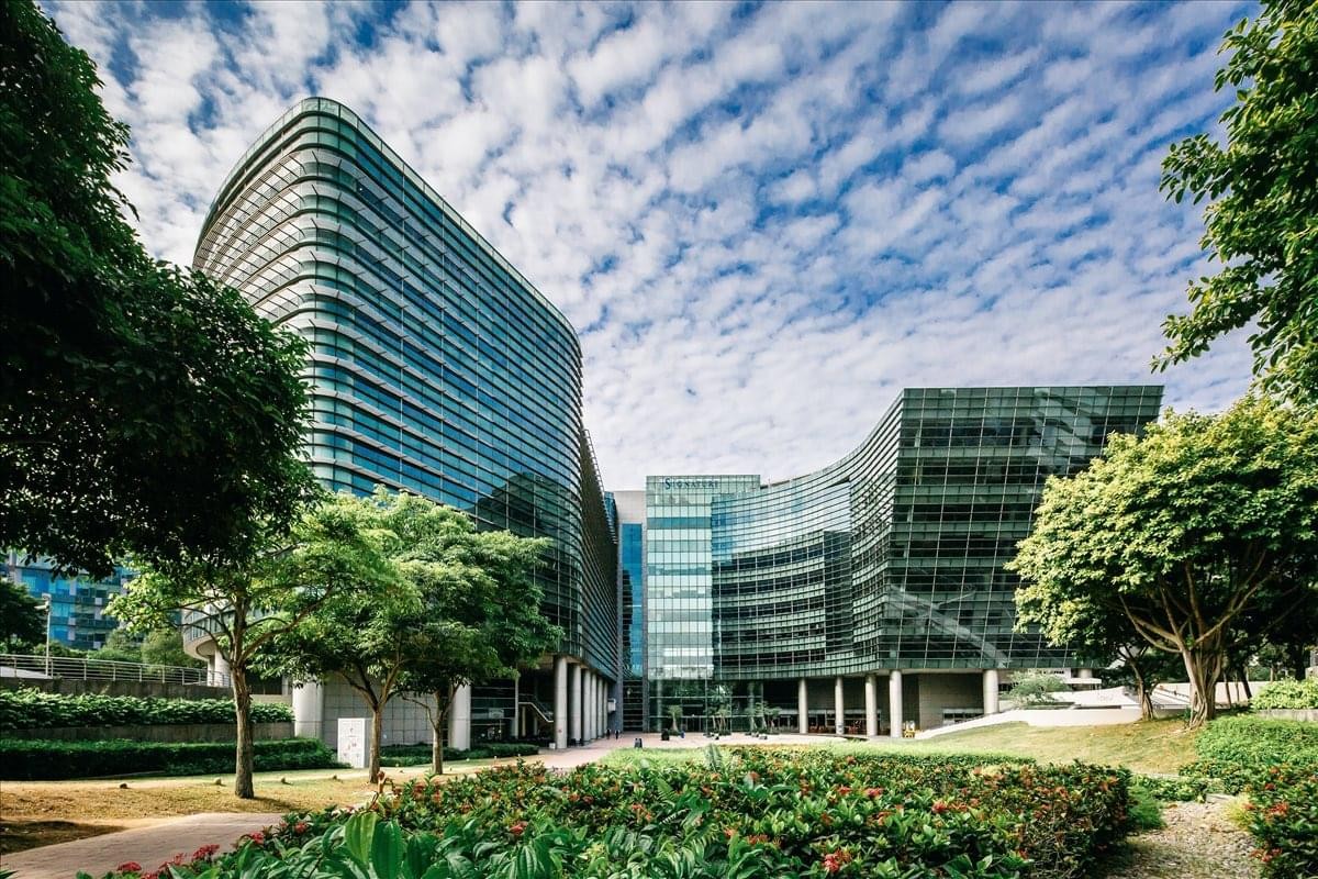 Modern glass facade of The Signature building at Changi Business Park surrounded by lush green trees.