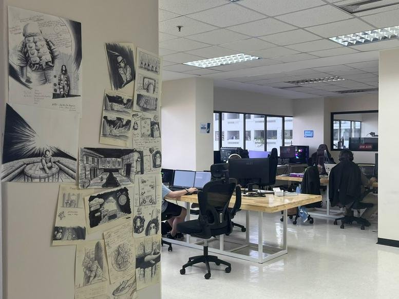 Open-plan office at BB Building with sketches on the wall and wooden desks with computer monitors.