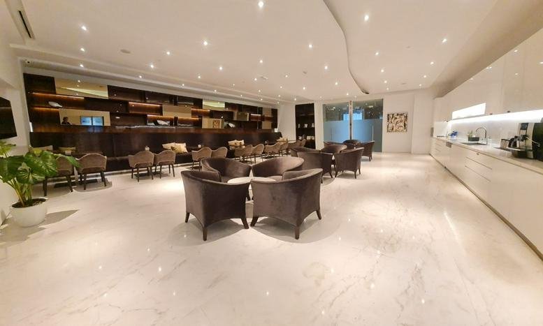 Spacious communal lounge with white marble floors and modern dark armchairs at 56 Floor, Jalan Jendral Sudirman Kav 86.