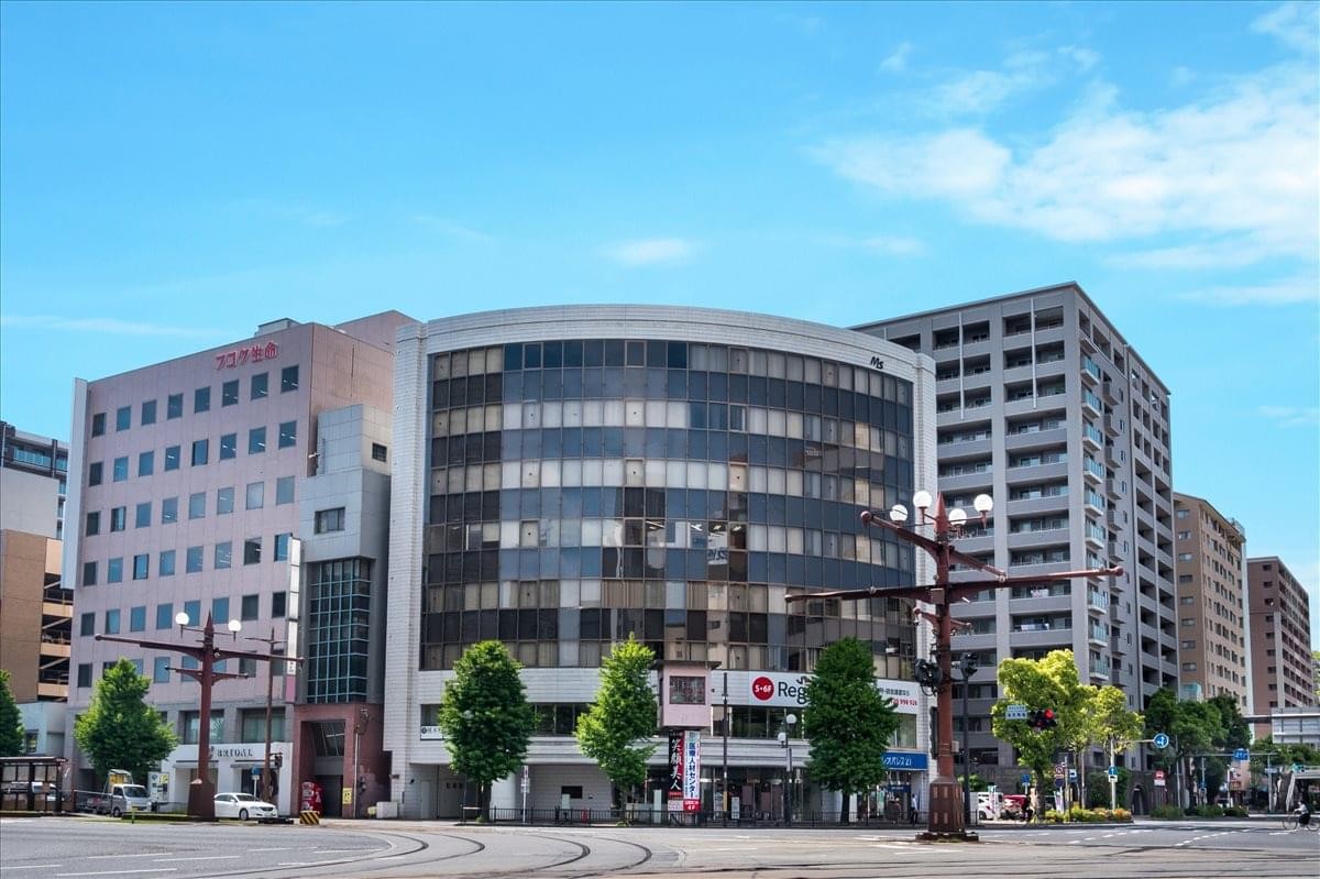 Exterior view of the curved glass facade of the Kagoshima MS Building under a blue sky.