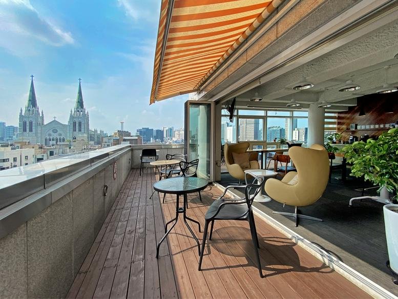 Rooftop terrace at Seoul Bldg with wooden decking, seating, and views of church spires.