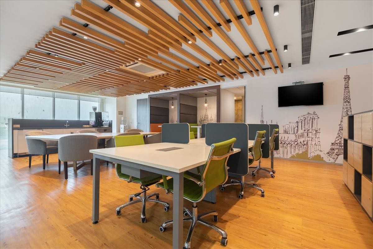 Bright coworking area featuring wooden slat ceiling, green chairs, and an Eiffel Tower wall mural.
