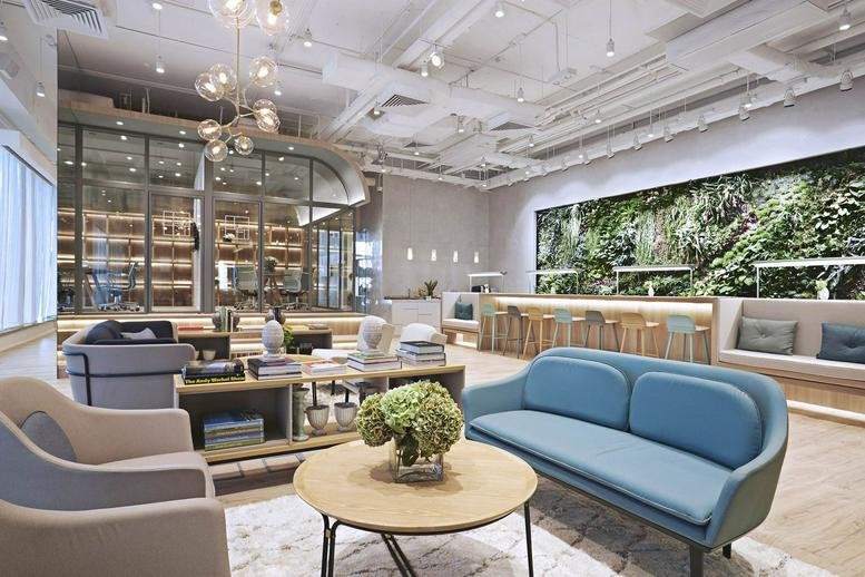 Spacious communal lounge at 6a Shenton Way with blue sofas and a large lush vertical garden wall.