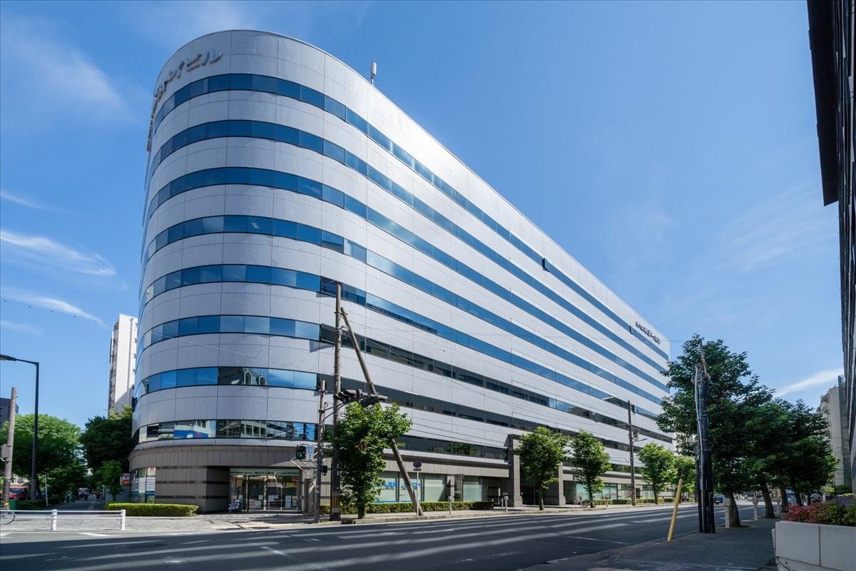 Exterior view of the curved facade of 6F Shin Osaka Dai 3 Doi Building against a blue sky.