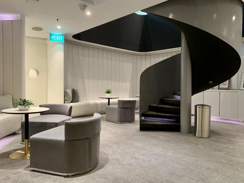 Sleek modern lounge at 75 High Street, Singapore featuring a black spiral staircase and plush grey seating.