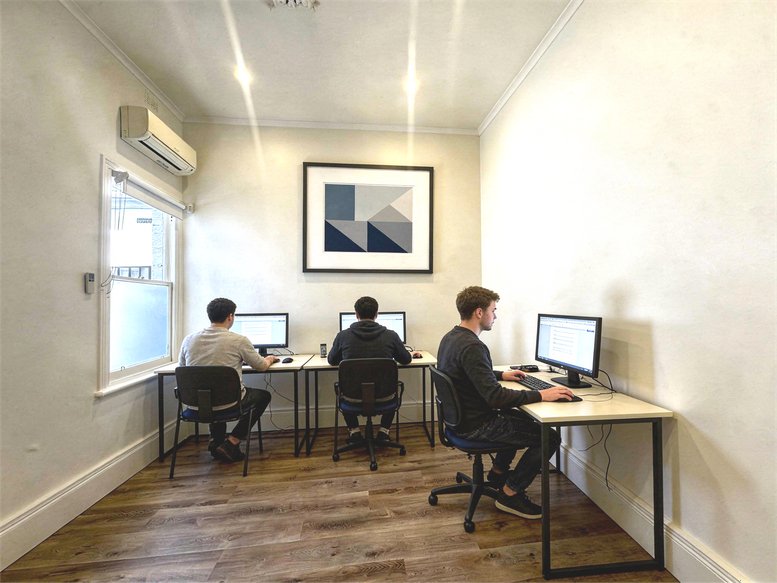 Spacious three-person office with large desks, ergonomic chairs, and modern geometric wall art.