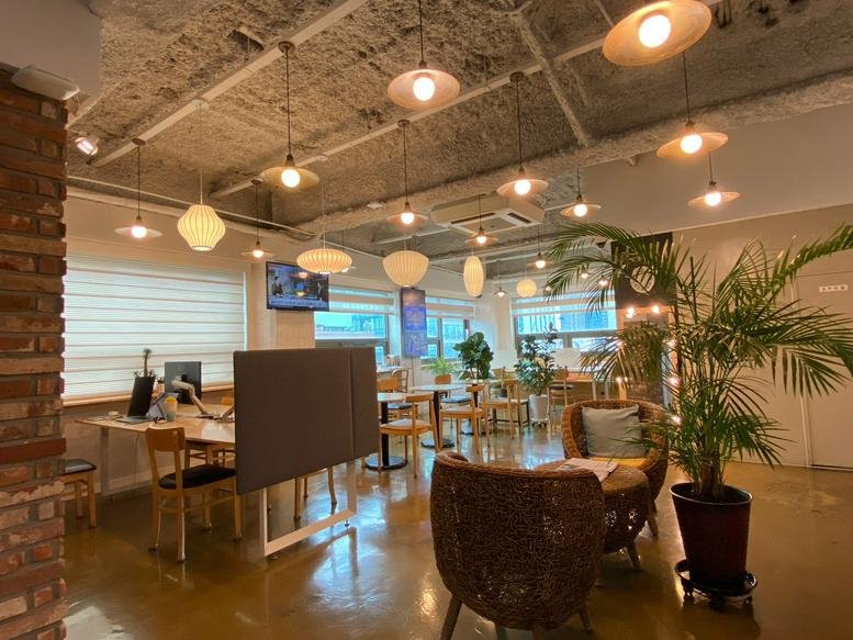 Vibrant common lounge at Aimhigh Tower with exposed ceilings, hanging lamps, and potted palms.