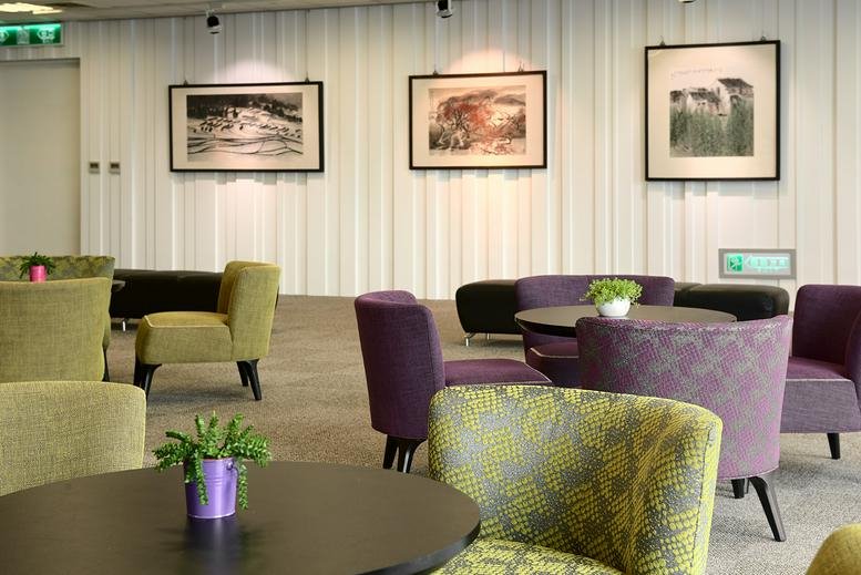 Bright lounge area with purple and lime green armchairs and framed artwork.