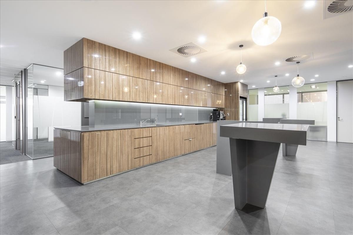 Modern communal kitchen and breakout area with wood-grain cabinetry and island benches.