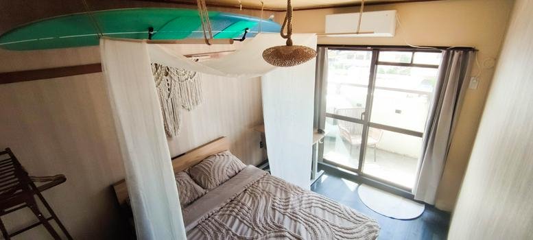 Isahama Seaside Mansion Suite A605 bedroom with a hanging surfboard and natural light.