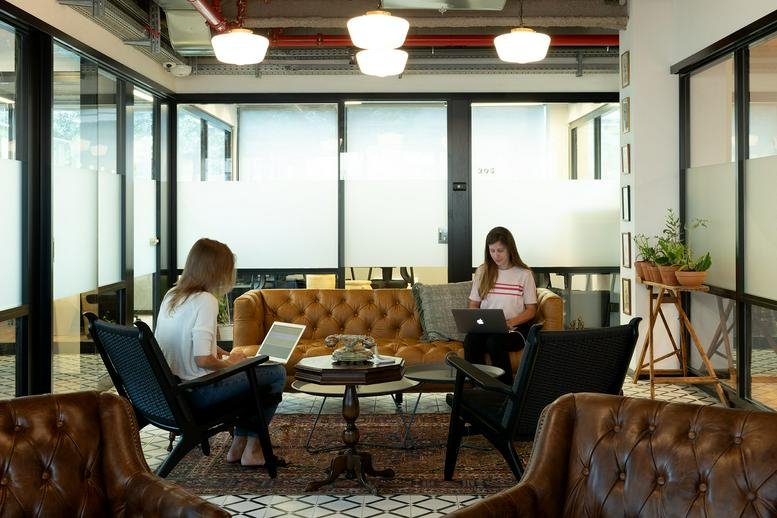 Bright breakout lounge at Ahad Ha’am 54 St with tan leather sofas and glass-walled private offices.