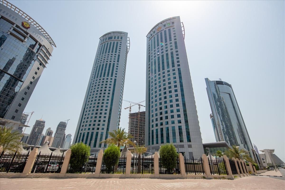 Exterior view of the twin glass-and-stone skyscrapers of Al Fardan Towers under a clear sky.