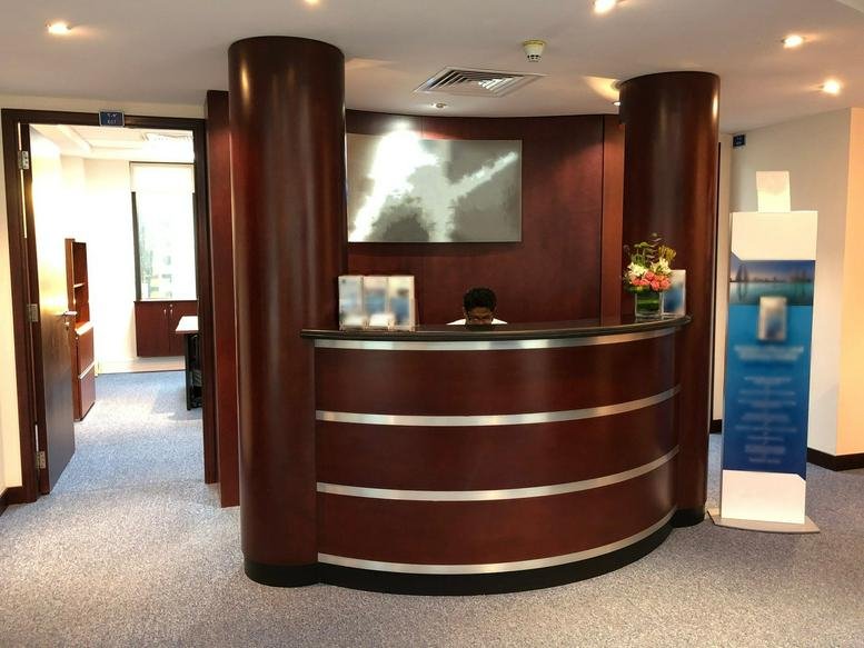 Warm wood-paneled reception area at Al Jasrah Tower with a curved desk and soft overhead lighting.