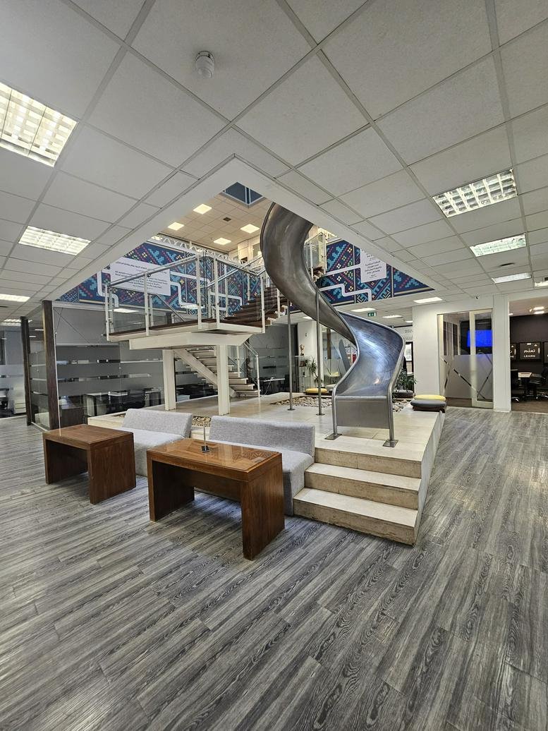 Modern breakout area with a unique metal slide, wooden coffee tables, and contemporary seating.