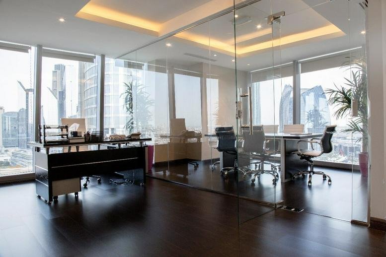 Executive office with glass partitions, dark wood flooring, and city views.