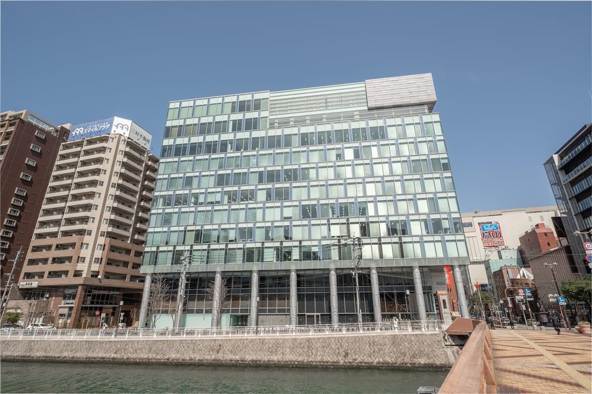 Exterior view of the multi-story glass and concrete Aqua Hakata building by the waterfront.
