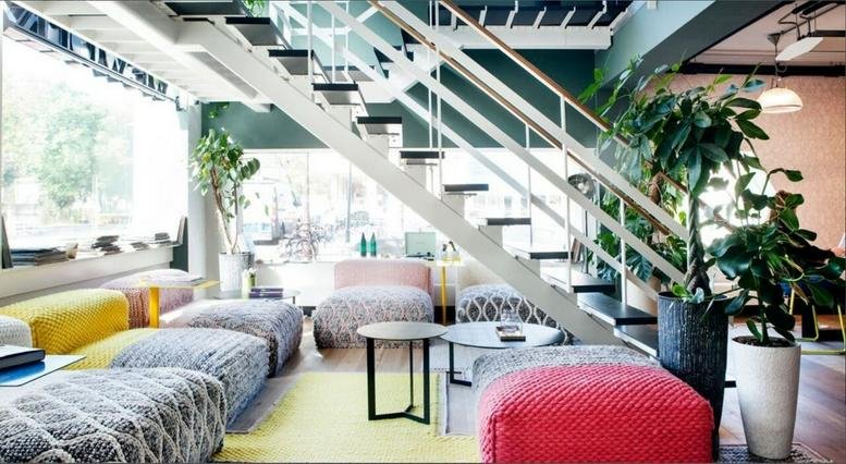 Spacious communal lounge at Arekere Village, Begur Hobli Bannerghatta Road featuring colorful poufs and a staircase.