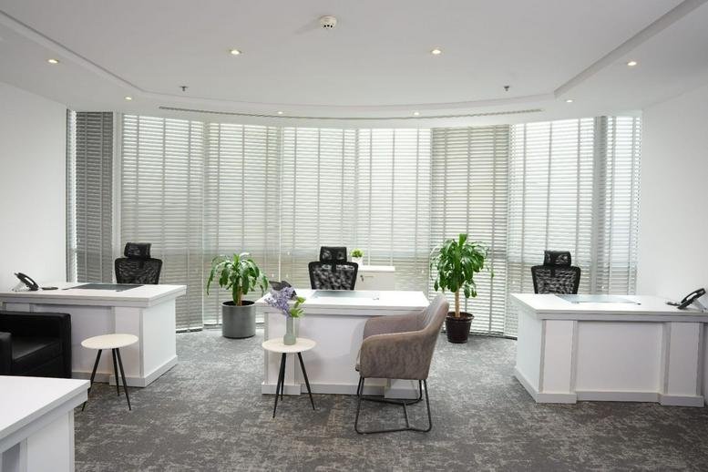 Bright open-plan office with three white desks, executive chairs, and indoor plants.