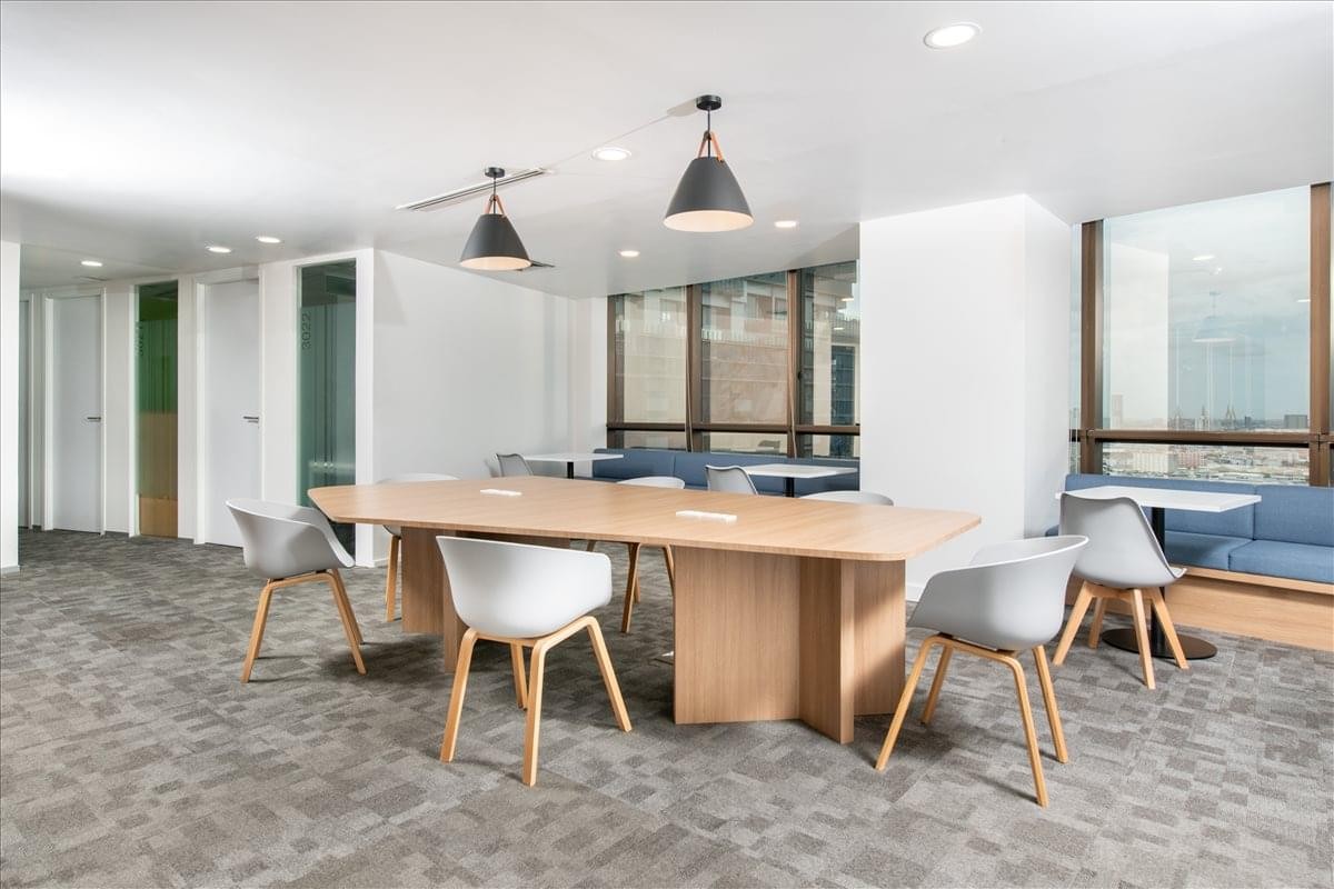 Contemporary coworking space with long wooden tables, stylish pendant lighting, and blue booth seating.