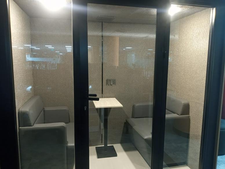 Small glass-enclosed meeting booth with grey seating and a small pedestal table.