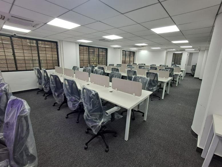 Open-plan workspace with multiple desks and plastic-covered chairs.