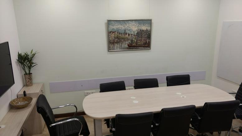 Spacious conference room featuring a long oval table, black office chairs, and framed artwork on the wall.