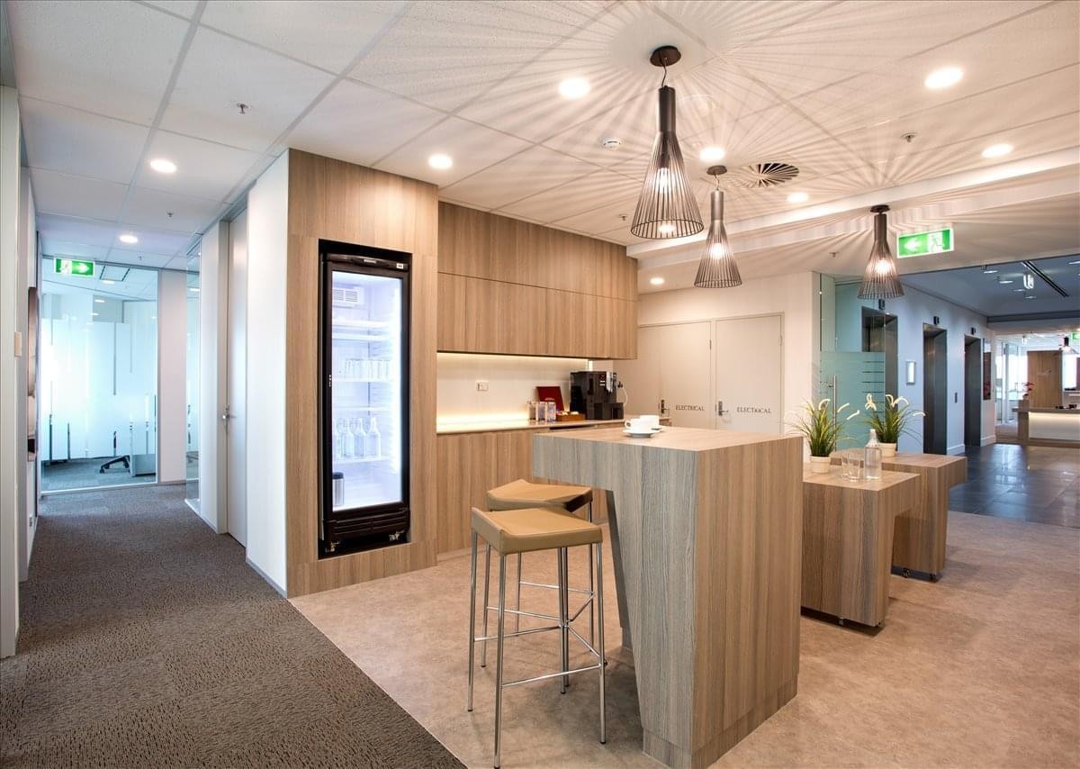 Modern communal kitchen with light wood cabinetry and a breakfast bar with stools.