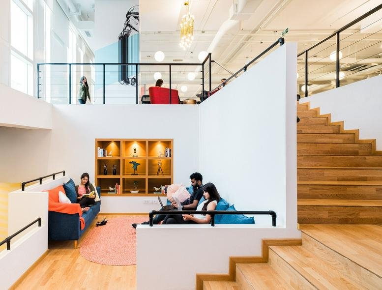 Spacious bi-level lounge at CoWrks Whitefield, Block 1B, RMZ NXT, with wooden stairs and natural light.