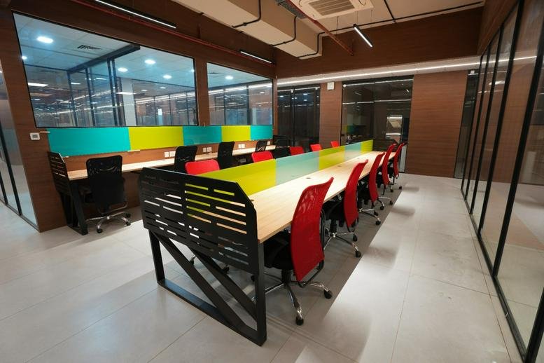 Long coworking table with vibrant red chairs and colorful desk dividers.