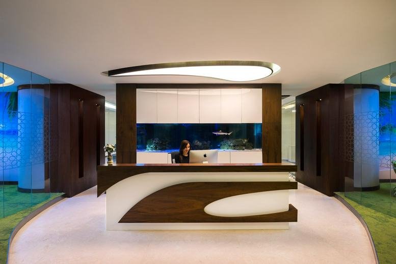 Bright reception area at Düsseldorf Business Point featuring a curved wood-accented desk and aquarium.