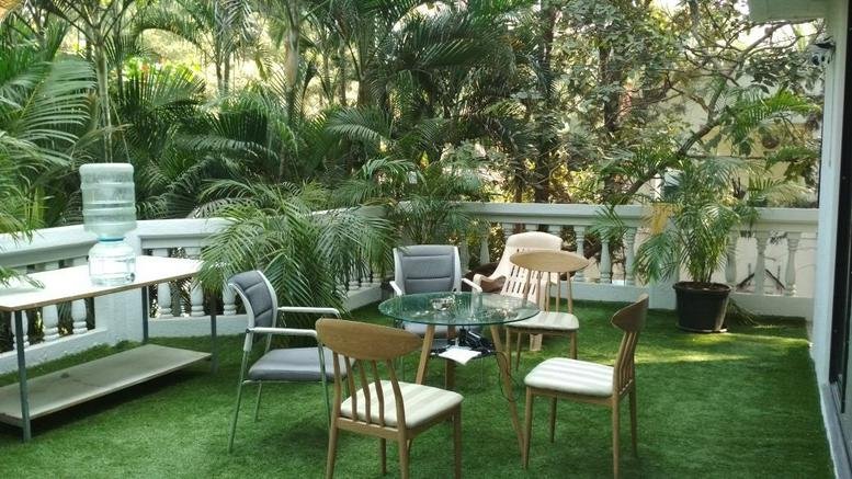 Lush outdoor terrace at D27, Varsha Park featuring artificial grass, wooden chairs, and dense tropical greenery.